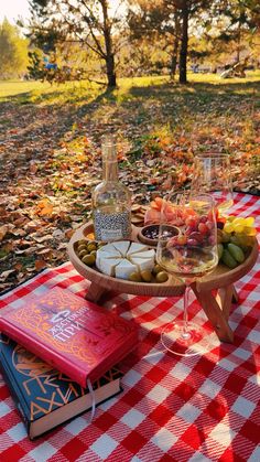 an outdoor picnic with food and drinks on the table in the fall leaves, along with two wine glasses