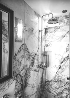 black and white photograph of a marble bathroom with shower head, mirror, and faucet