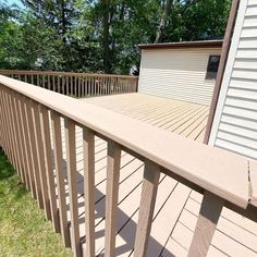 a wooden deck in front of a house with grass on the ground and trees behind it