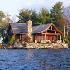 a house sitting on top of a lake next to a shore covered in rocks and trees