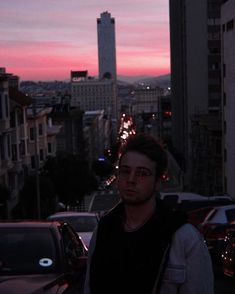 a man standing in the middle of a parking lot at dusk with his cell phone up to his ear