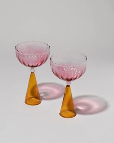 two pink glass goblets sitting next to each other on a white table top