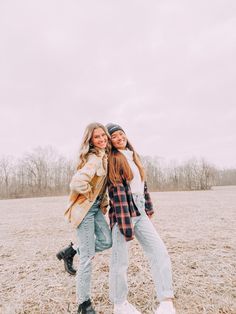 two girls are standing in the middle of an open field, one has her arms around the other