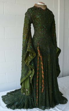 a green dress on display in front of a white brick wall with a coat hanging from it's back