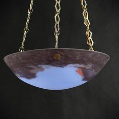 a glass hanging from chains on a black background with the reflection of clouds in it