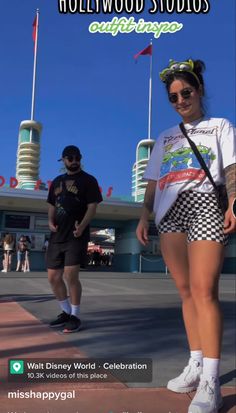 two people walking down the street in front of a building with hollywood studios on it