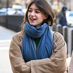 a woman wearing a blue scarf and jacket walking down the street with her arms crossed