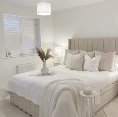 a bed with white linens and pillows in a bedroom next to a lamp on the wall