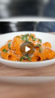 a white bowl filled with pasta covered in sauce and parsley on top of a wooden table