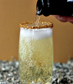 someone is pouring champagne into a glass with ice and gold flakes on the rim