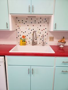 a kitchen with blue cabinets and red counter tops is pictured in this image, there is a sink that has colorful tiles on the wall behind it