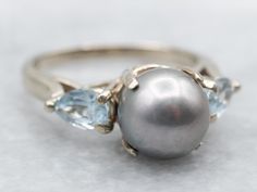 Truly timeless, this pearl ring has a beautifully polished white gold band, and pear-cut accent aquamarines set on each side of the pearl. The saltwater pearl has a lavender luster with pink undertones and makes the perfect understated piece. Metal: 14K White GoldGem: Gray Saltwater PearlGem Measurements: 8.4 mm, RoundAccents: 2 Aquamarine totaling .76 CaratsRing Size: 5.75Marks: "14K*" Stamped on the inside band Elegant Pear Shaped Topaz Ring, Elegant Silver Pear-shaped Moonstone Ring, Elegant Pear-shaped Topaz Ring For Formal Events, Elegant Pear Shaped Topaz Ring For Formal Occasions, Pearl Engagement Ring, Saltwater Pearls, Aquamarine Engagement Ring, Aqua Marine, White Gold Band