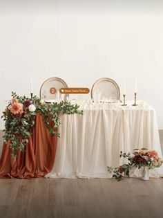 the table is set up with two chairs and an orange cloth draped over it, surrounded by greenery