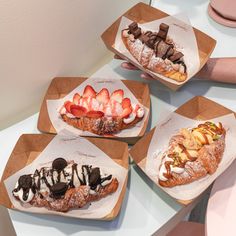 four different types of pastries are on display in paper trays with toppings