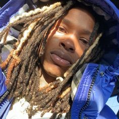 a young man with dreadlocks on his head and wearing a blue jacket in the sun