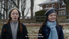 two women standing next to each other in front of a house with snow on the ground