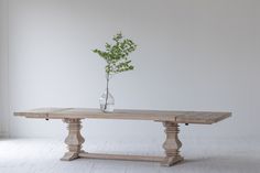 a wooden table with a vase on it and a small plant in the middle, against a white wall