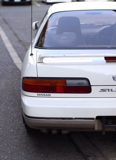 the back end of a white car parked on the side of the road next to a parking meter