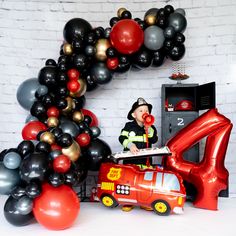 a fireman next to balloons in the shape of an arch and a red car