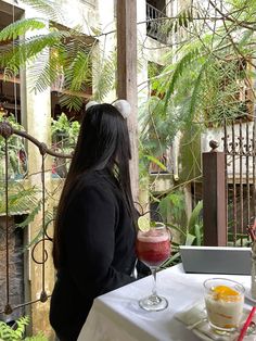 a woman sitting at a table with food and drink in front of her, looking out the window