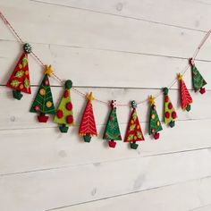 a string of christmas trees hanging on a white wooden wall with red and green decorations