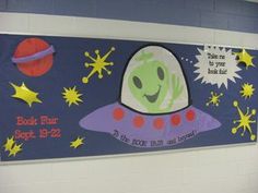 a bulletin board with an alien on it in a school hallway, decorated with stars and the words book fair