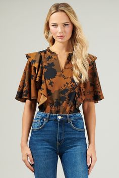 Elevate those everyday outfits when you add the Sandy Floral Ruffle Blouse to your wardrobe! This blouse boasts a chic floral print throughout, shaping flutter short sleeves with a split neckline and some ruffles. You can wear it with any shorts or pants and tuck it in or leave as is and achieve a cute fit! - Split neck- Flutter sleeves- Ruffles- Relaxed fit- Color: Brown BlackSize + Fit - Model is 5'8" and wearing size XS- Measurements taken from size S - Chest: 18 1/2"- Length: 25" Fabric Self Flutter Sleeve Top With Floral Print For Work, Fitted Floral Print Blouse With Flutter Sleeves, Chic Blouse With Floral Print And Butterfly Sleeves, Fall Floral Print Blouse With Flutter Sleeves, Flutter Sleeve Blouse With Floral Print For Fall, Floral Print Short Sleeve Blouse For Work, Short Sleeve Blouse With Floral Print For Work, Workwear Blouse With Floral Print And Flutter Sleeves, Fall Ruffle Hem Short Sleeve Blouse