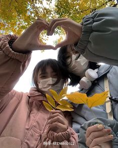 two people wearing face masks are making a heart shape with their hands while holding a leaf