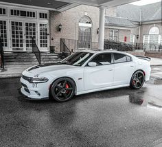 the white dodge charger is parked in front of a brick building on a rainy day