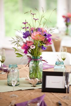 a vase filled with purple and pink flowers sitting on top of a table next to two empty glasses