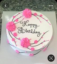 a white cake with pink flowers on it that says happy birthday written in black lettering