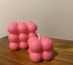 two pink candles sitting on top of a wooden table next to each other and one candle is shaped like an apple