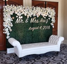 a white bench sitting in front of a green wall with flowers on it and mr and mrs rug