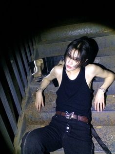 a young man sitting on the steps with his hand in his pocket and wearing a black tank top