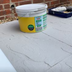 a yellow bucket sitting on top of a cement floor next to a white tub filled with dirt