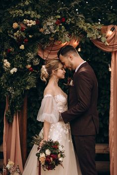 a bride and groom standing in front of a floral arch