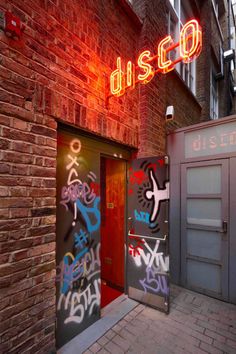 two doors with graffiti on them in front of a red brick building that says disco