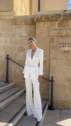 a woman standing in front of some steps wearing a white suit and heels with her hands on her hips