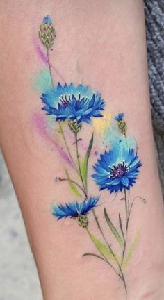 a blue flower tattoo on the right thigh and leg, with watercolor flowers painted on it