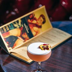 a cocktail sitting on top of a table next to an open book