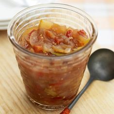 a jar filled with food sitting on top of a wooden table next to a spoon