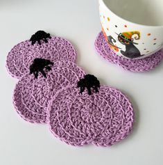 three crocheted coasters with black cats on them next to a coffee cup