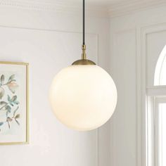 a light fixture hanging from the ceiling in a living room with white walls and paintings on the wall