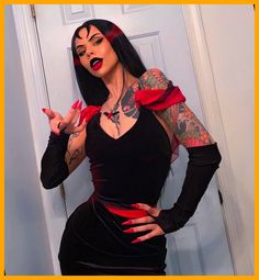 a woman dressed in black and red with tattoos on her arms, holding out her hands