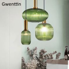 three green glass pendant lights hanging from the ceiling above a table with flowers on it