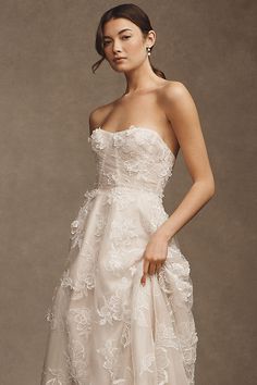 a woman in a strapless wedding dress poses for a photo with her hand on her hip