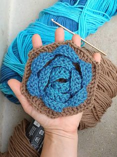 someone is holding up a crocheted blue and brown object in front of two skeins of yarn