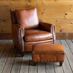 a brown leather chair and ottoman in front of a wooden wall