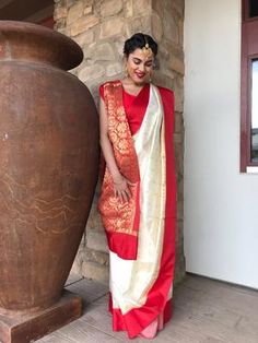 a woman in a red and white sari standing next to a large brown vase