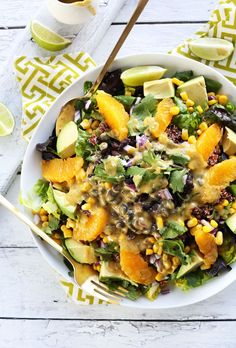 a white bowl filled with salad and topped with avocado, oranges and other vegetables